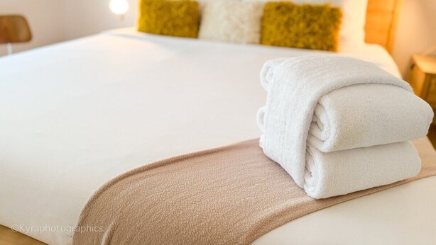 Una cama bien hecha con sábanas blancas y una toalla blanca doblada al lado.