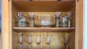 Un aparador de madera con varios estantes que contienen diferentes tipos de cristalería, incluyendo copas de vino y vasos grandes.