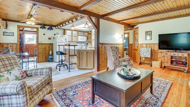 A spacious living room with a wooden ceiling, a television, a dining area with a table and chairs, and a kitchen in the background. - Near Mississippi River! Countryside Family Retreat (Eastman)