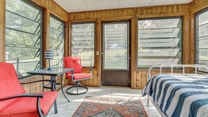 A bedroom with a bed, a red chair, a table, and large windows. - Near Mississippi River! Countryside Family Retreat (Eastman)