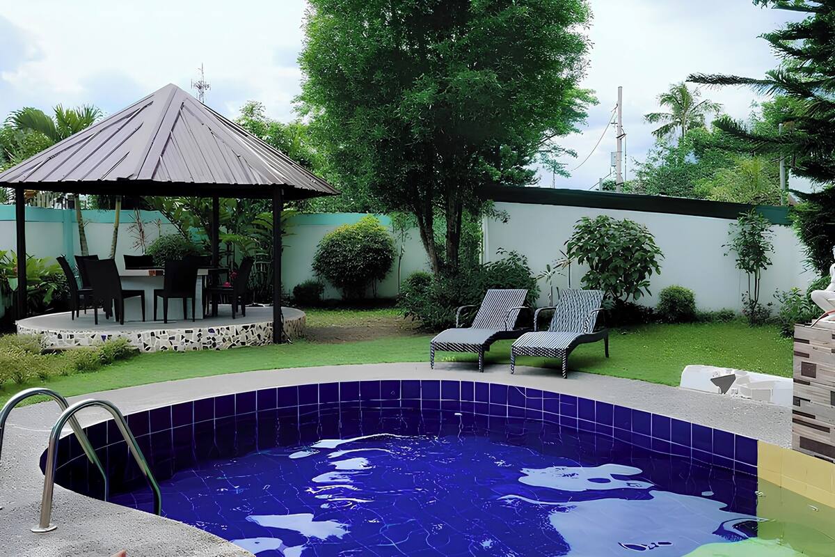A swimming pool with a tiled edge, surrounded by a patio area with chairs and a gazebo.