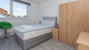 Quarto com cama, uma cadeira verde, guarda-roupa de madeira e janela com vista para edifícios.