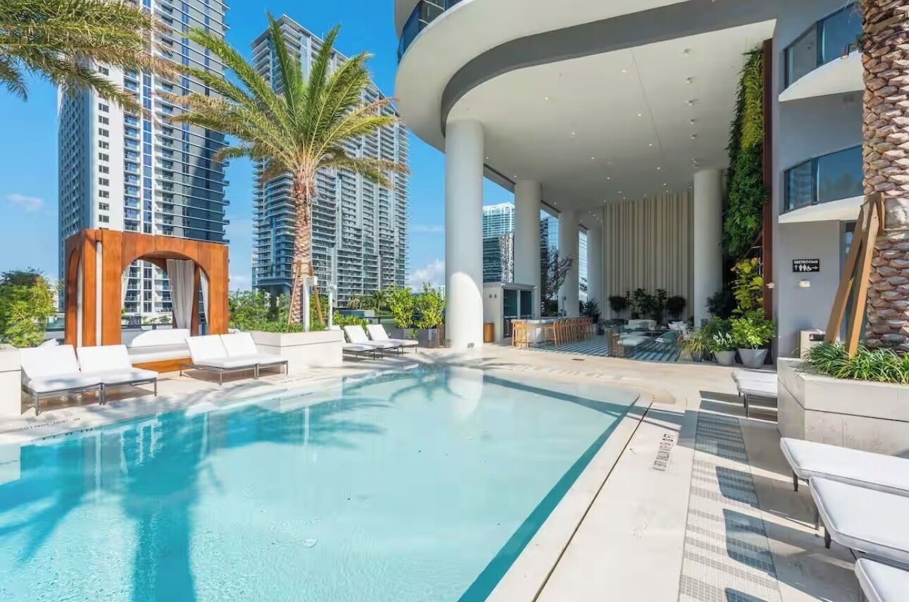 A modern hotel pool area with lounge chairs, a pool, and tall buildings in the background.