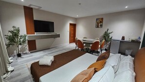 Habitación de hotel con una cama grande, un escritorio, una silla, una pequeña cocina y un televisor montado en la pared.