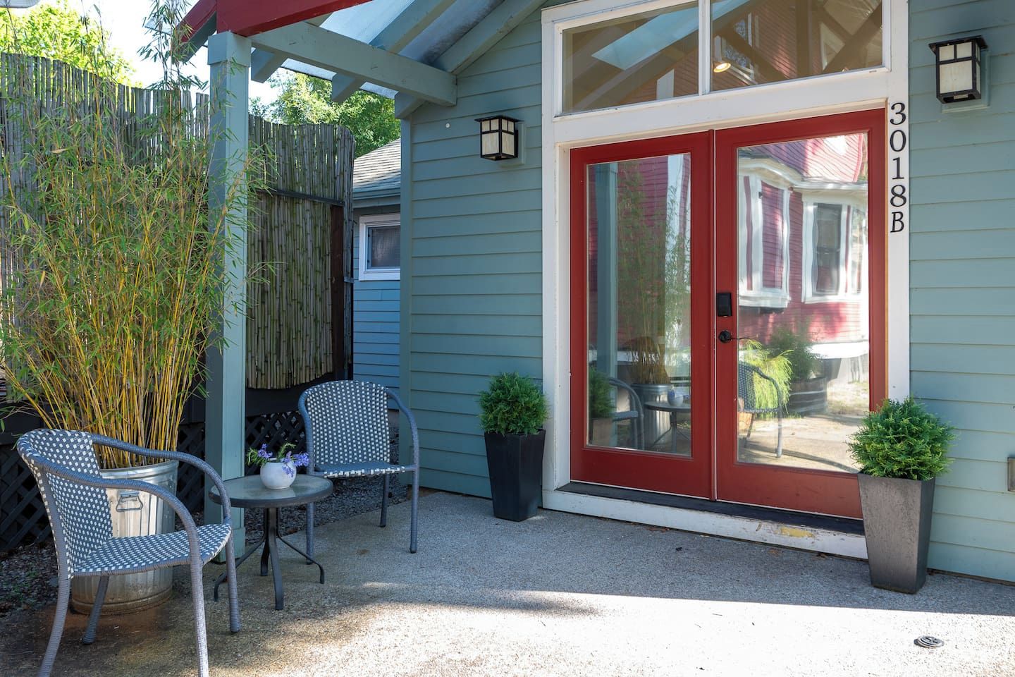 A house with a red door, a covered patio with two chairs, and a bamboo fence.