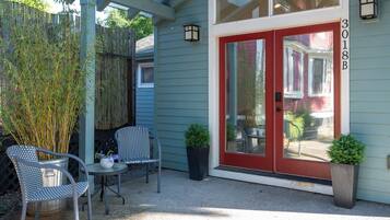 A house with a red door, a covered patio with two chairs, and a bamboo fence.