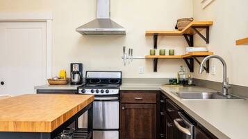 A compact kitchen with a stove, oven, and dishwasher, wooden table, and built-in shelves.