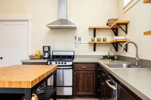 A compact kitchen with a stove, oven, and dishwasher, wooden table, and built-in shelves.