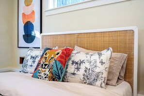 A bed with a woven headboard, multiple pillows with tropical and animal prints, and a framed abstract artwork above the bed. - Sunlit Laurelhurst Cottage - Office, Dog-Friendly (Portland)