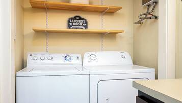 A laundry room with two white washing machines, wooden shelves, and a sign that reads 'The Laundry Room Loads of Fun.'