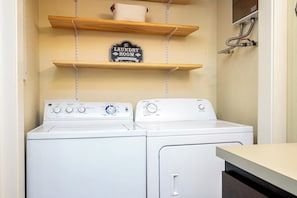 A laundry room with two white washing machines, wooden shelves, and a sign that reads 'The Laundry Room Loads of Fun.' - Sunlit Laurelhurst Cottage - Office, Dog-Friendly (Portland)