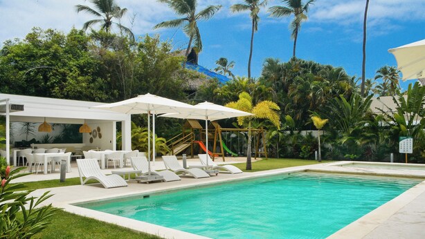 A swimming pool with lounge chairs and umbrellas, surrounded by lush greenery and palm trees. - Luxury 2BR apartment steps from the beach (Punta Cana)