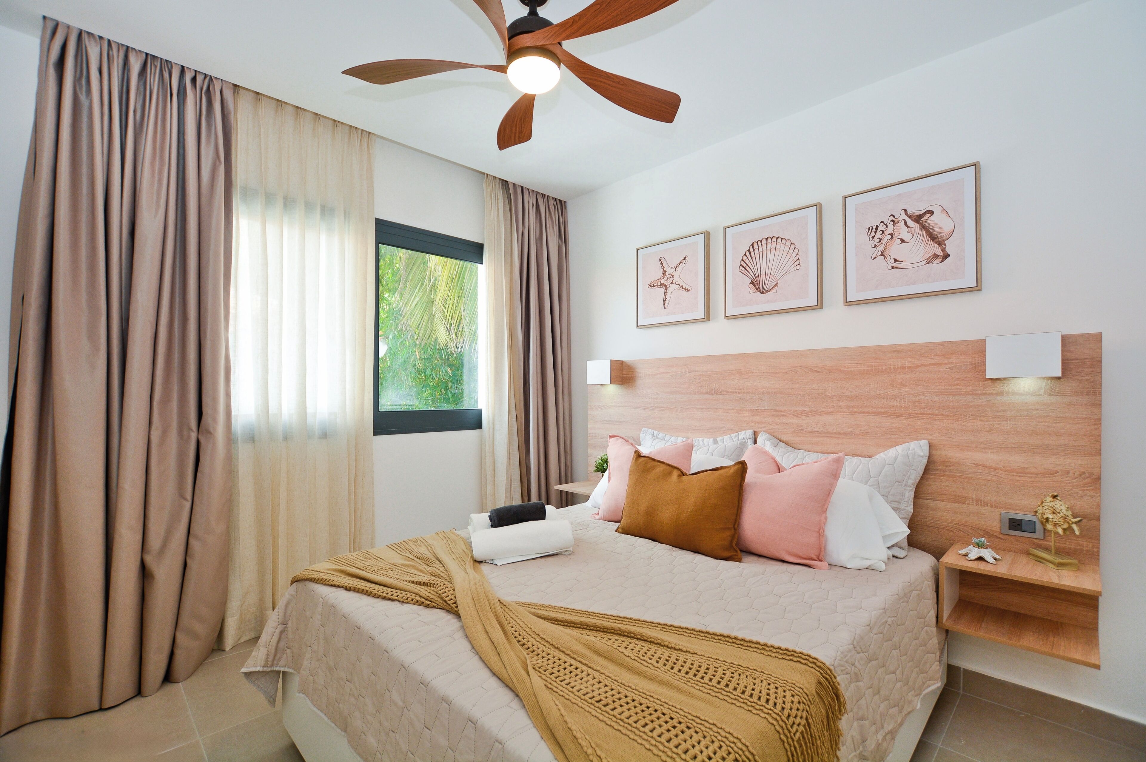 Een slaapkamer met een bed, gordijnen, een plafondventilator en wanddecoratie.