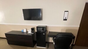A hotel room with a flat-screen TV mounted on the wall, a small desk with a microwave, a black office chair, and a brown sofa. - Rusina inn (Colorado Springs)