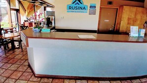 A reception desk with a sign for 'Rusina Inn & Suites' and a 'Cash Customers' sign. There are chairs and tables in the background, and a door labeled 'Employee Only'. - Rusina inn (Colorado Springs)