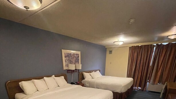 A hotel room with two beds, a framed picture on the wall, and a window with curtains. - Rusina inn (Colorado Springs)
