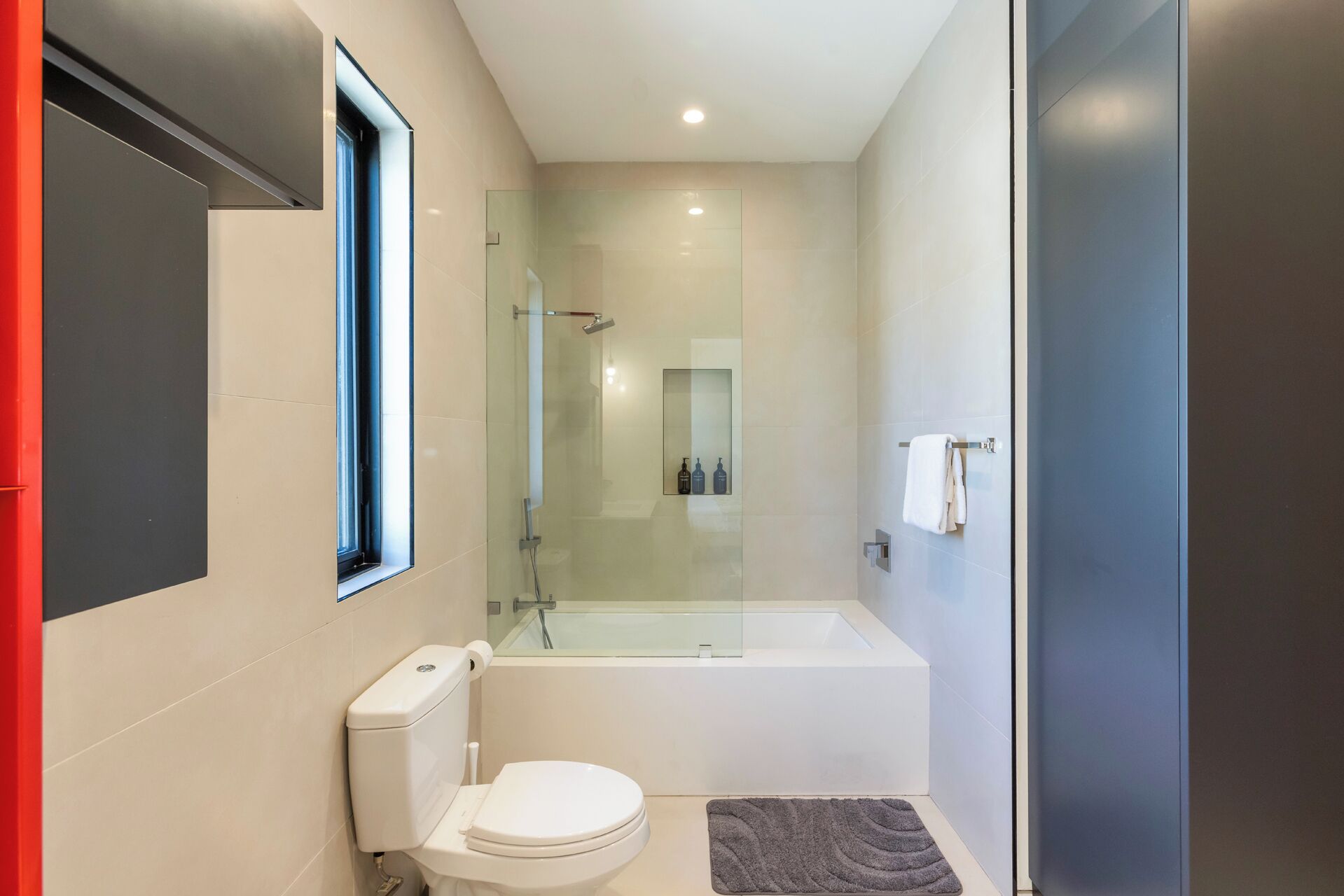 A modern bathroom with a toilet, a glass-enclosed shower, and a bathtub.
