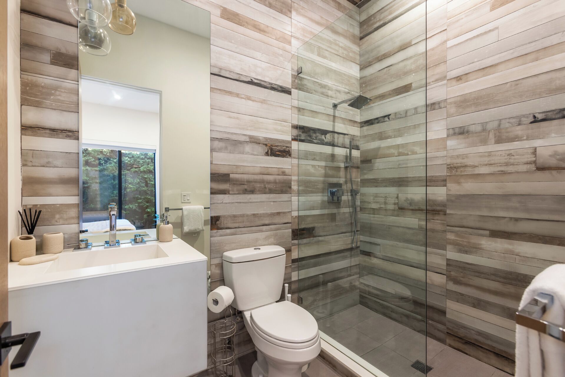 Een moderne badkamer met een douchecabine van glas, een witte wastafel en een toilet.