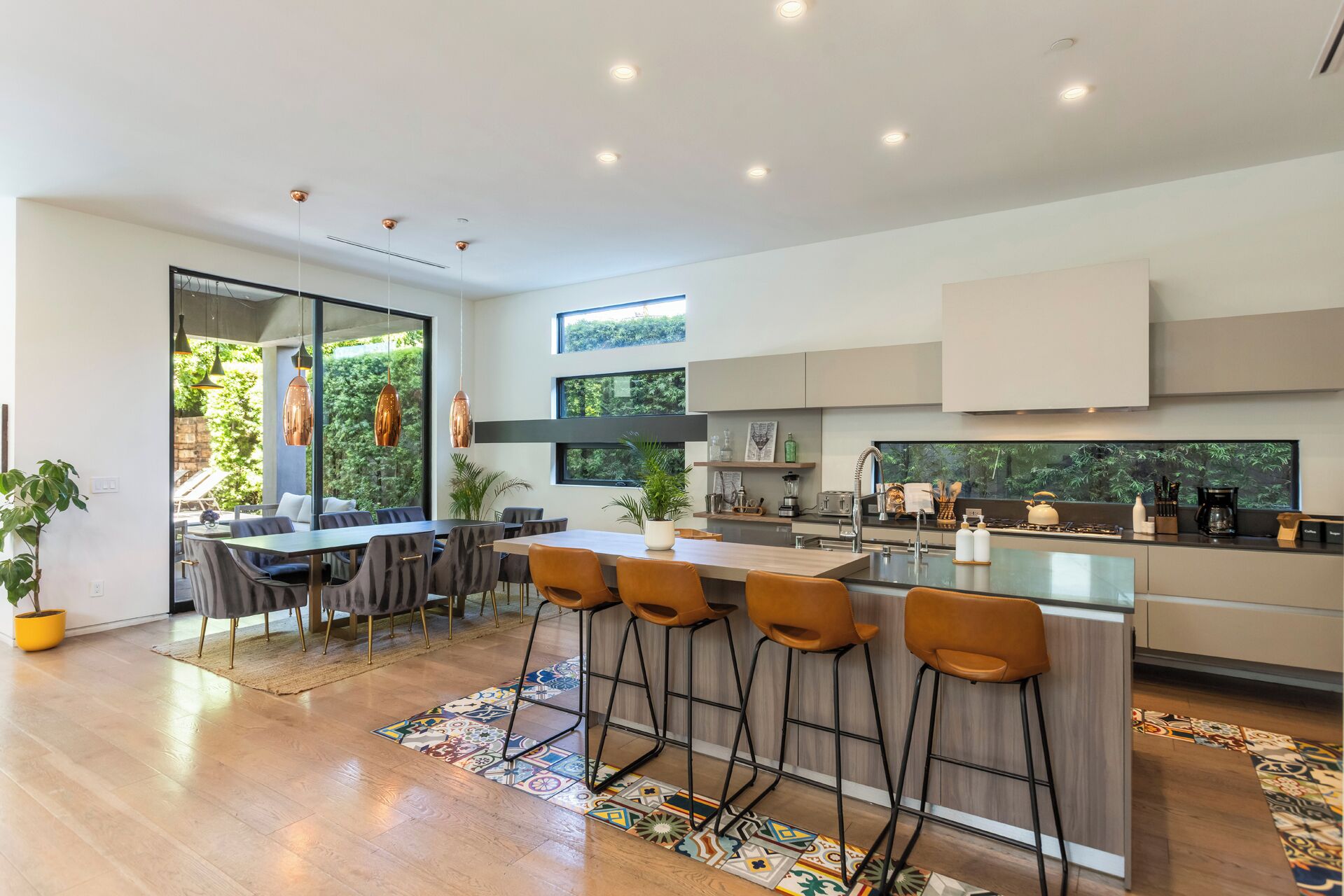 Een moderne keuken met een centraal eiland, barstoelen en een eethoek met een groot raam dat uitkijkt op groen.