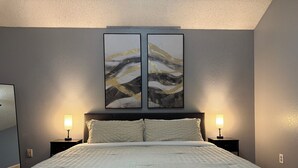A bedroom with a bed, two bedside tables, and two wall-mounted lamps. - Cozy 4 bedroom home in Grand Prairie,TX (Grand Prairie)