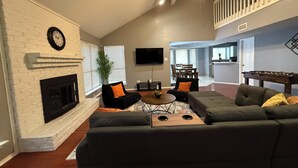 A spacious living room with a fireplace, a ceiling fan, and a dining area in the background. - Cozy 4 bedroom home in Grand Prairie,TX (Grand Prairie)