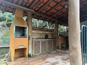 An outdoor kitchen area with a grill, a wine bottle, and a wooden cabinet. - Ecolodge Paraty-Mirim site for up to 22 people (Paraty-Mirim)