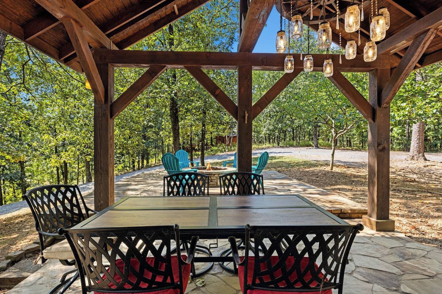 Eine überdachte Terrasse im Freien mit Tisch und Stühlen, umgeben von Bäumen.