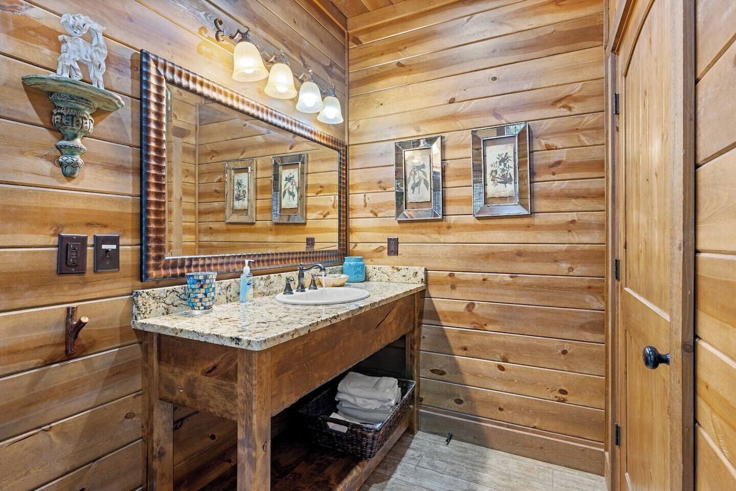 Un baño de cabaña de madera con tocador de madera, un espejo grande y fotografías enmarcadas en la pared.