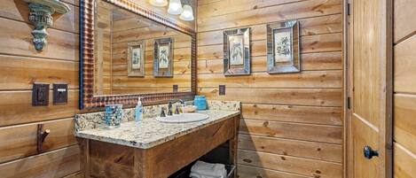 Un baño de cabaña de madera con tocador de madera, un espejo grande y fotografías enmarcadas en la pared.