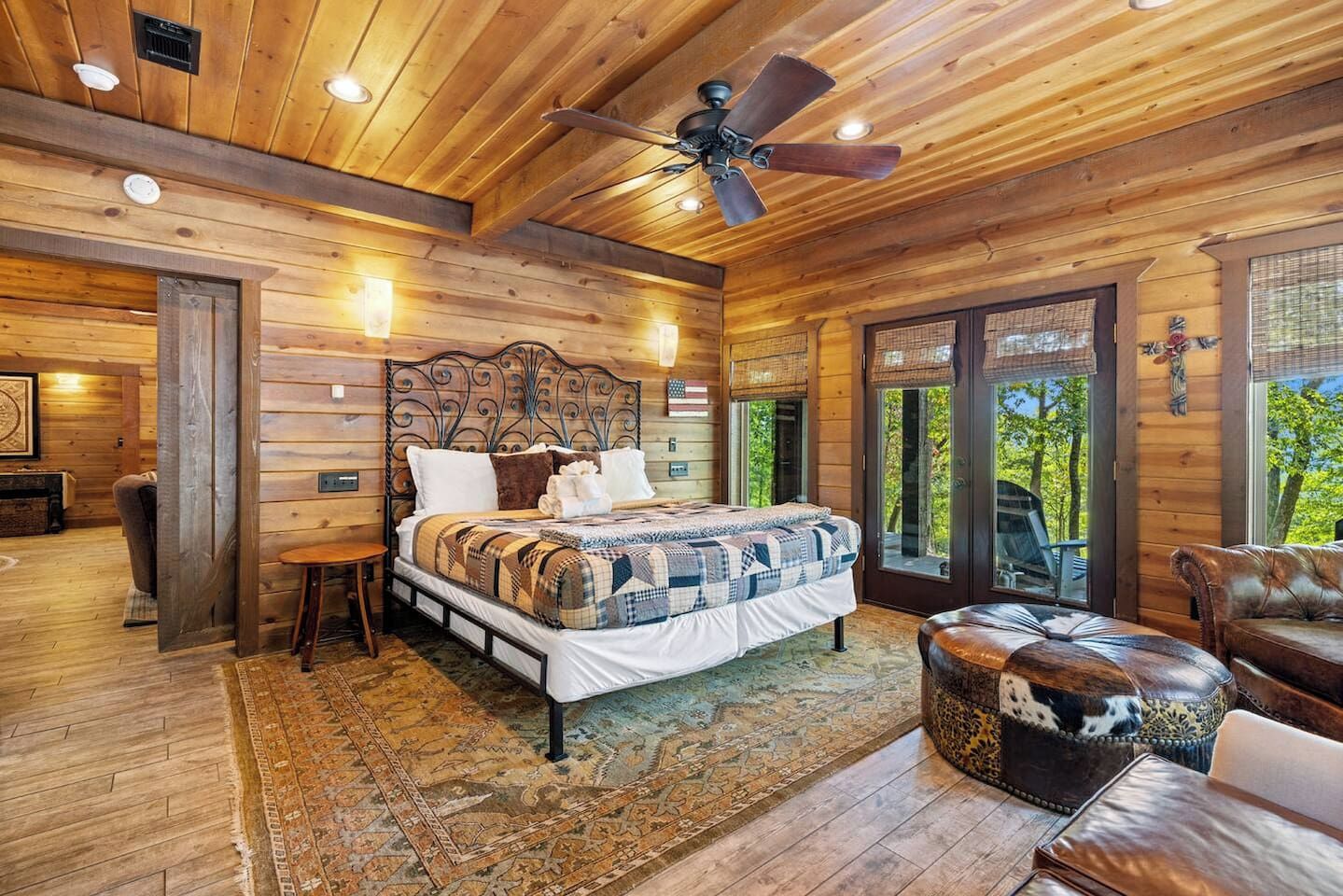 Een houten slaapkamer met een groot bed, een plafondventilator en uitzicht op de omgeving.