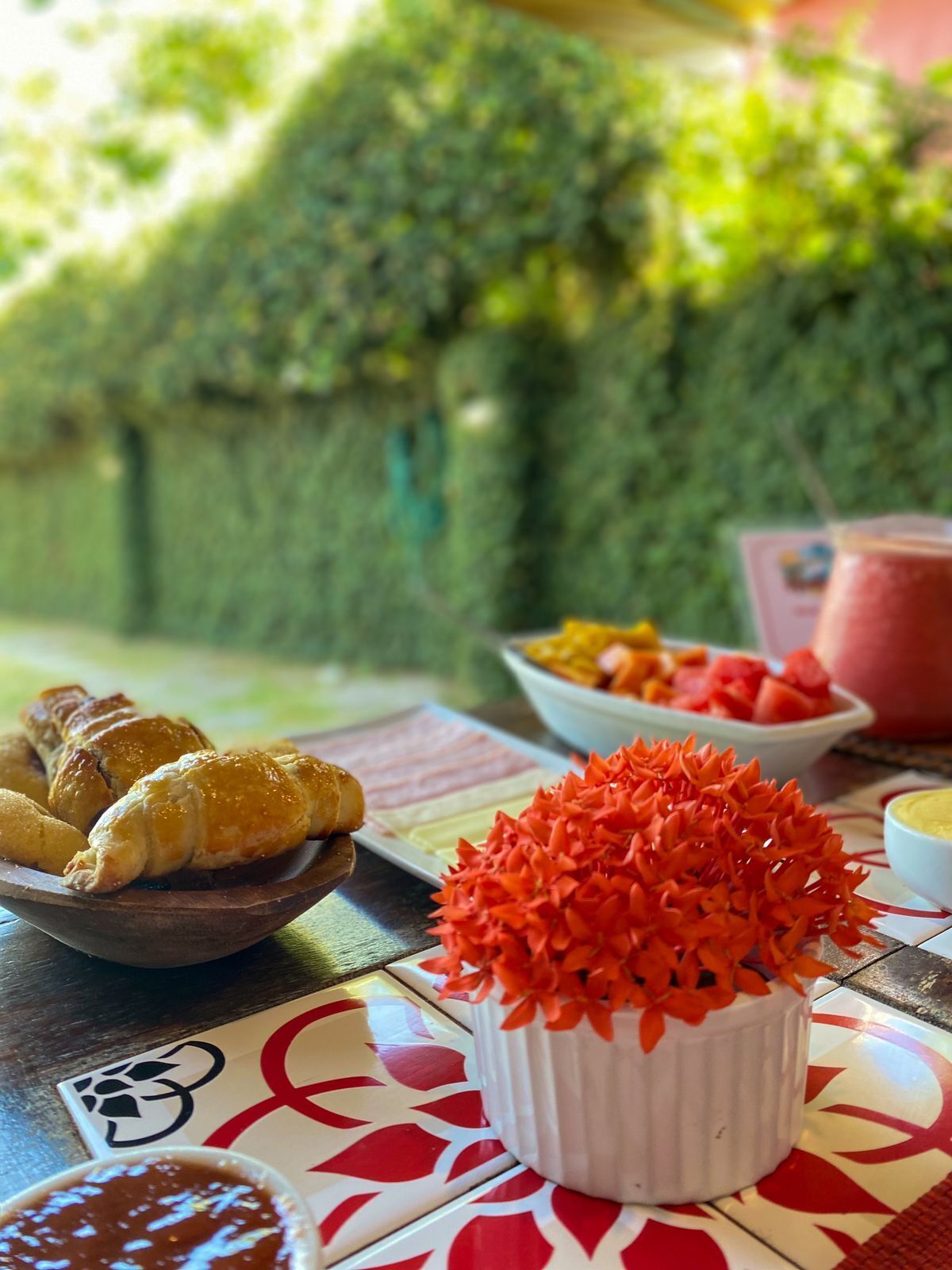 Uma mesa com croissants, uma tigela de legumes cortados e um vaso decorativo.