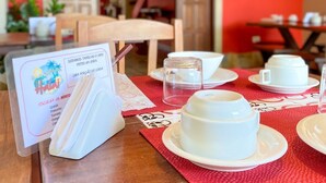 Ein Tisch ist gedeckt mit weißen Tassen und Untertassen, einer Speisekarte und einer roten Tischmatte in einem Raum mit roten Wänden und einer Holztür.