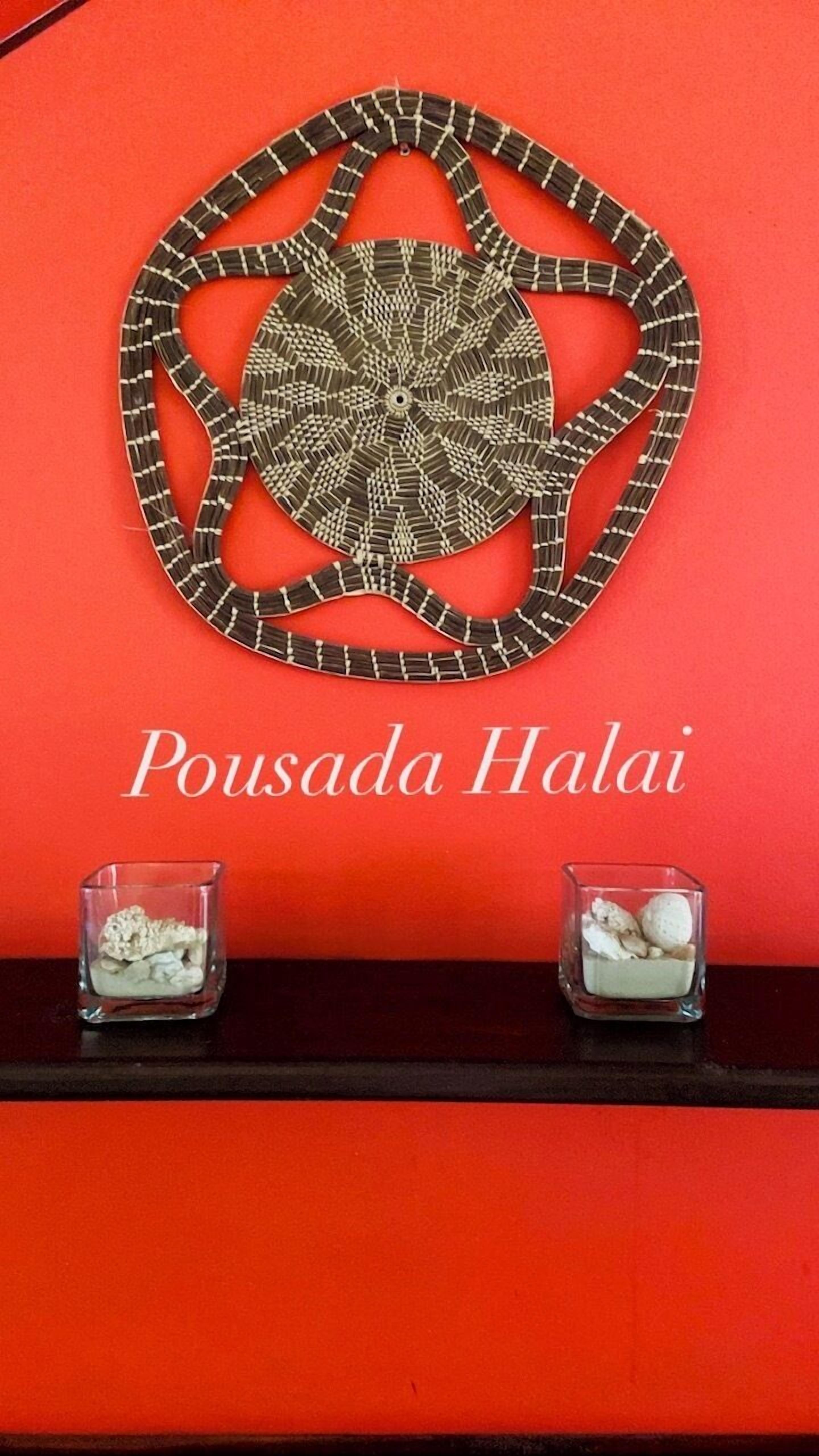 Una pared con un adorno circular y el texto "Pousada Halai" sobre un fondo rojo.