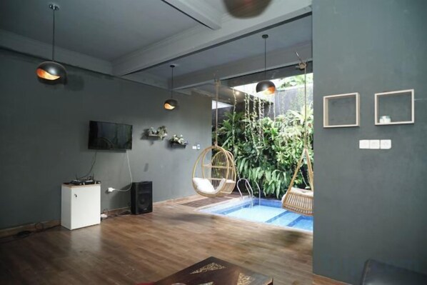 Un interior moderno con suelo de madera, luces colgantes, un televisor y un sillón colgante.