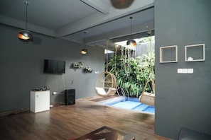 Un interior moderno con suelo de madera, luces colgantes, un televisor y un sillón colgante.