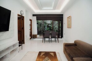 Una sala de estar moderna con un televisor de pantalla plana, un sofá, un comedor con sillas y un ventanal grande.