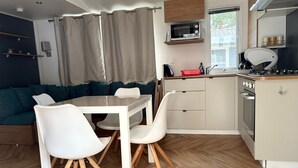 A compact kitchen with a microwave, stove, and sink. There is a dining table with chairs and a sofa in the background. - Mobile home 6/8 pers camp 4 stars (Saint-Jean-de-Monts)