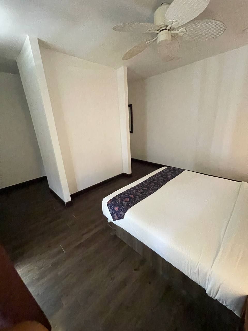 A room with a bed, a ceiling fan, and a wooden floor.