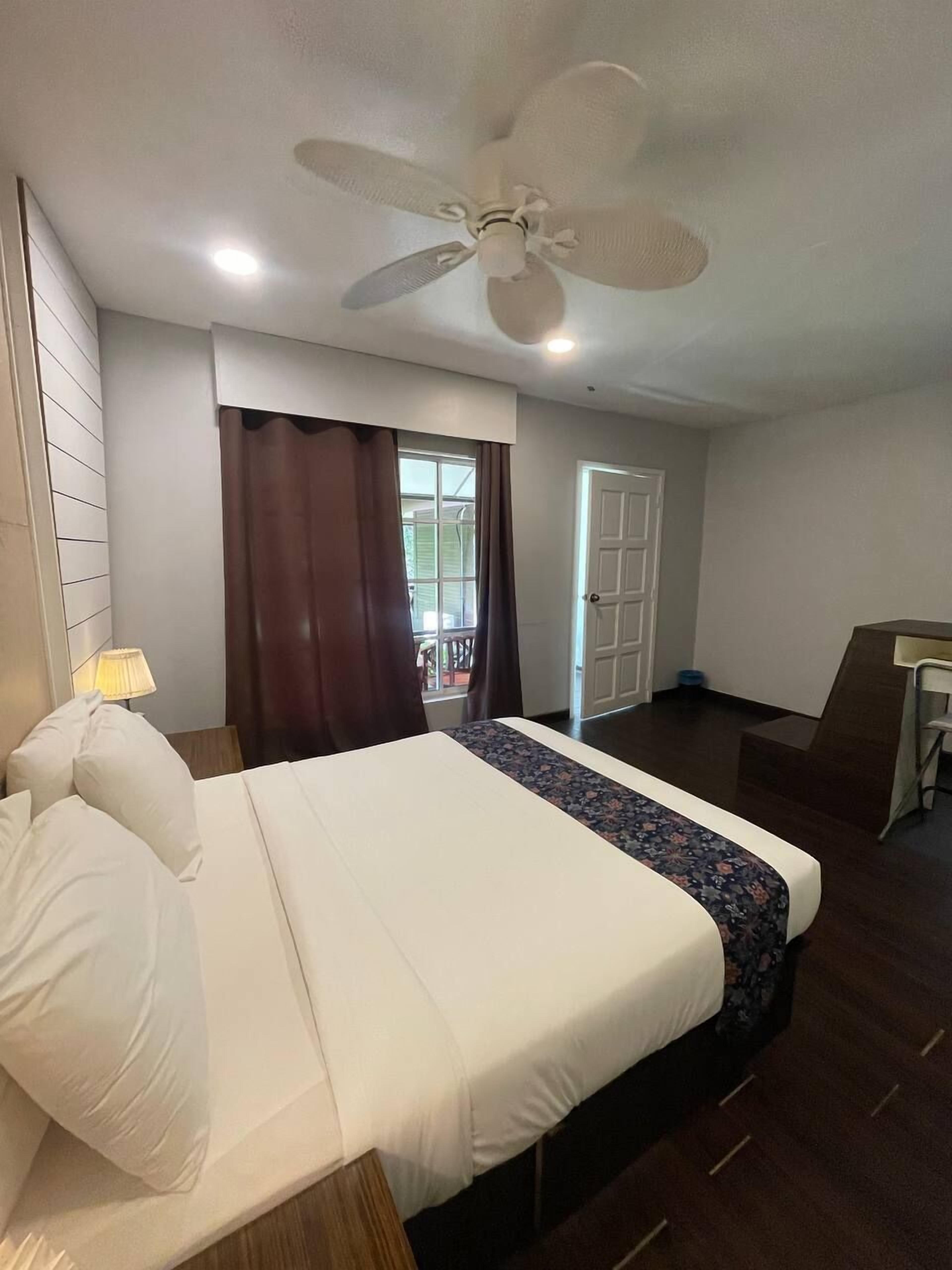 A hotel room with a bed, a desk, a ceiling fan, and a window with curtains.