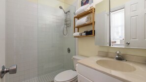 A bathroom with a glass-enclosed shower, a toilet, a sink with a mirror above it, and a towel rack with folded towels. - Authors Retreat (Key West)