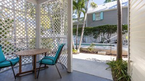 A covered patio with a wooden table and turquoise chairs, a pool in the background, and a white fence. - Authors Retreat (Key West)