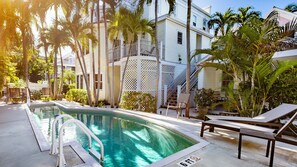 A pool area with a clear blue pool, lounge chairs, and palm trees. - Authors Retreat (Key West)