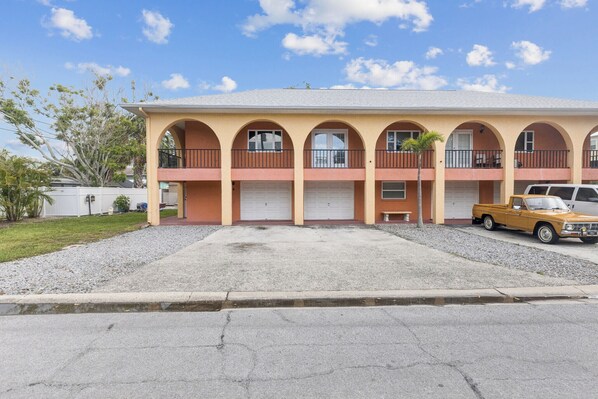 A two-story motel with a central courtyard, multiple balconies, and a vintage car parked in front.