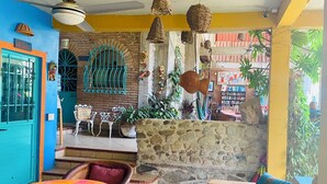 A cozy interior with a stone wall, colorful chairs, a table with a vibrant tablecloth, and hanging baskets.