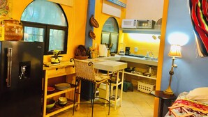 A compact kitchen with a refrigerator, microwave, and coffee maker. There is a dining table with chairs and a small sink.