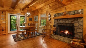 Interior acogedor de una cabaña con chimenea de piedra, una mesa de comedor de madera y sillas.