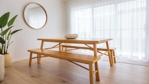 A wooden table with a bowl on top, a round mirror on the wall, and a potted plant to the left.