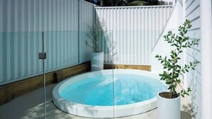 A circular hot tub with a glass enclosure, surrounded by a white fence, and a potted plant to the right.