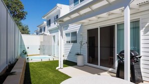A modern house with a patio, a barbecue grill, and a small pool.
