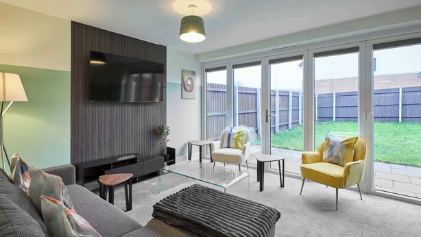 A modern living room with a flat-screen TV, a sofa, a coffee table, and a yellow armchair. - Modern Home in Quiet Environment (Corby)